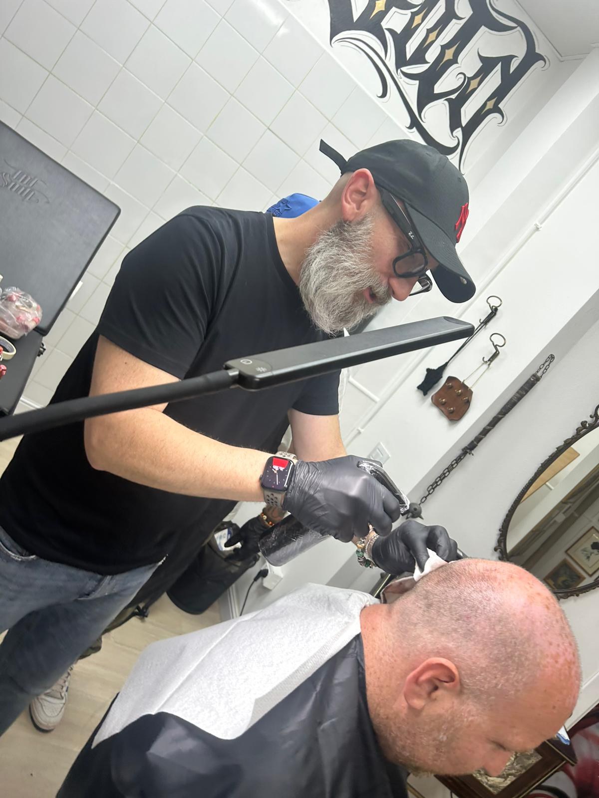 Operatore con barba grigia e guanti neri esegue tricopigmentazione su un cliente calvo da Saloon Kitch